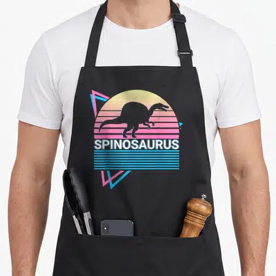 Spinosaurus dinosaur apron for women - Grey spinosaurus silhouette over pink and blue striped sun with geometric — shown on a black cotton canvas apron against a white background