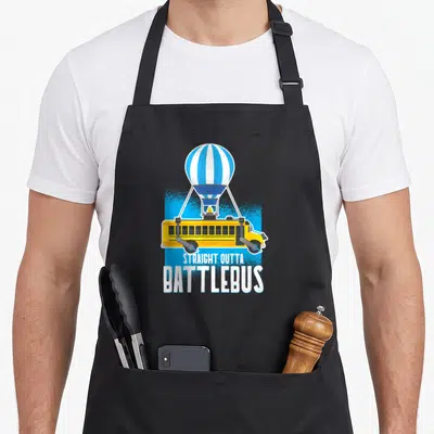 Straight battle royale apron - Yellow bus with wheel cannons suspended by blue white striped balloon with white text — shown on a black cotton canvas apron against a white background