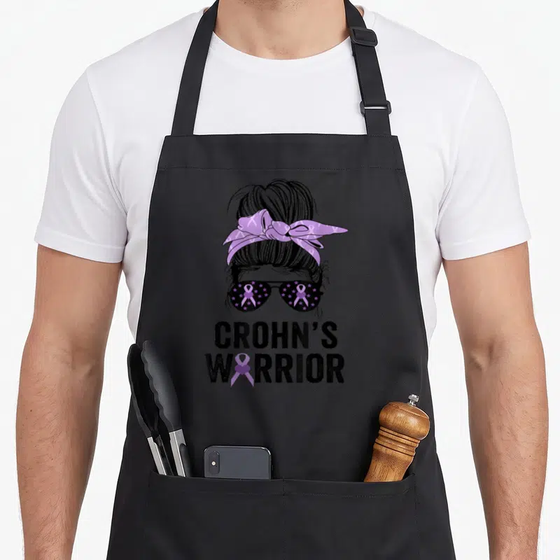 Crohn awareness ribbon apron - Stylized woman’s head with purple ribbon sunglasses and CROHN’S WARRIOR text — shown on a black cotton canvas apron against a white background