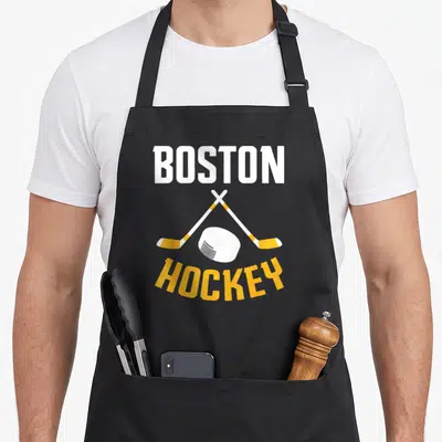 Boston hockey fan apron - BOSTON HOCKEY text with crossed sticks and puck in white and yellow — shown on a black cotton canvas apron against a white background