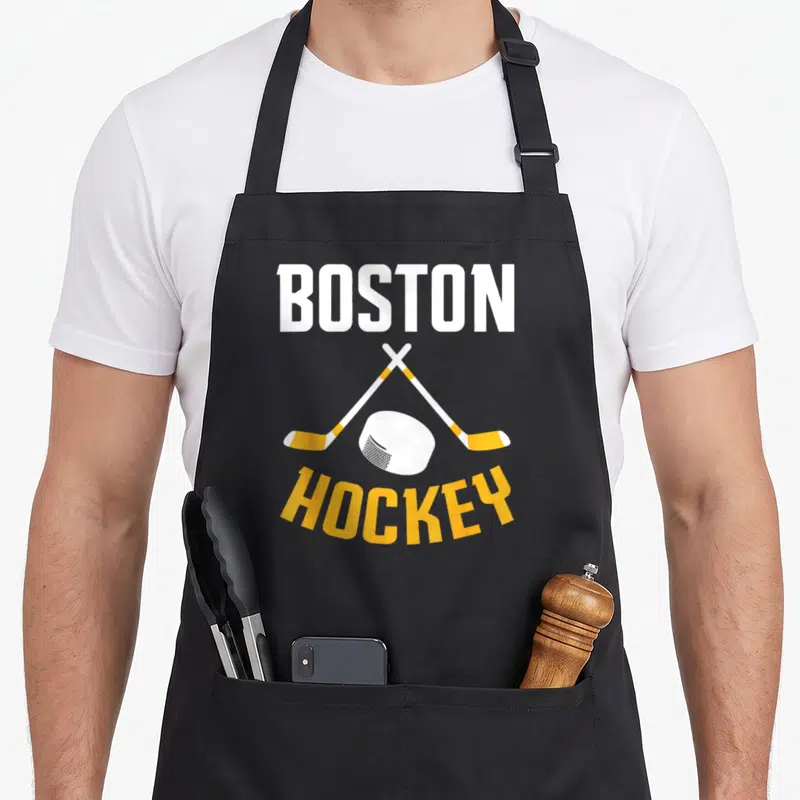Boston hockey fan apron - BOSTON HOCKEY text with crossed sticks and puck in white and yellow — shown on a black cotton canvas apron against a white background