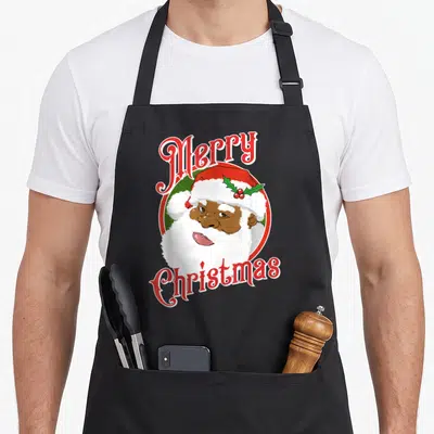 Merry santa claus apron - Cartoon Santa face with holly hat inside red and green circle with arched Merry Christmas text — shown on a black cotton canvas apron against a white background
