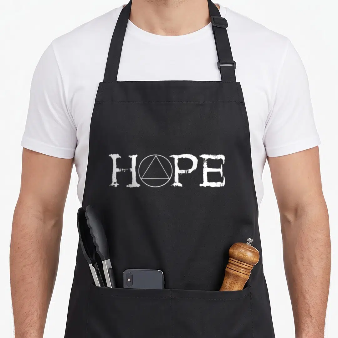 Hope sobriety apron - White HOPE text with circle and triangle symbol replacing the letter O — shown on a black cotton canvas apron against a white background