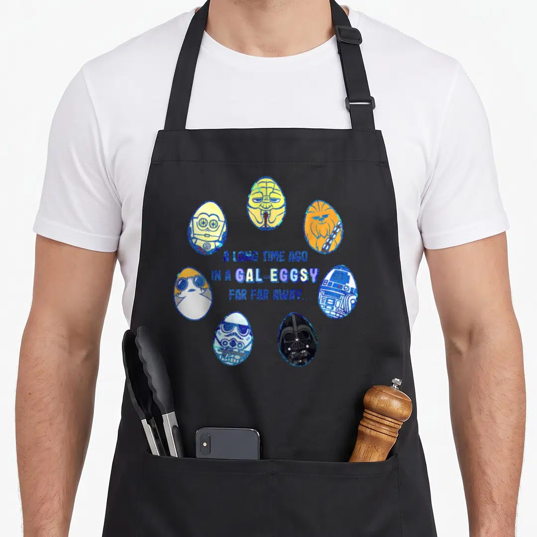 Gal easter apron - Seven Star Wars character eggs circle blue text reading Gal-Eggsy pun — shown on a black cotton canvas apron against a white background