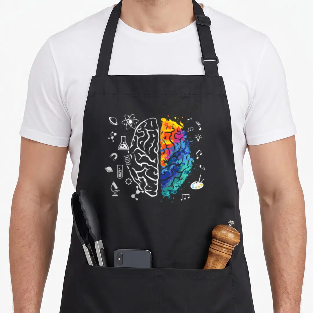 Brain science apron - Split brain with white science icons on left and multicolored art splash on right — shown on a black cotton canvas apron against a white background