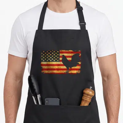 Fight us aprons - Grey rooster silhouette over distressed red white blue USA flag — shown on a black cotton canvas apron against a white background