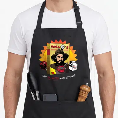 Torgo cereal apron - Cartoon cereal box with stern man, apple, milk carton, and text even the master would approve — shown on a black cotton canvas apron against a white background