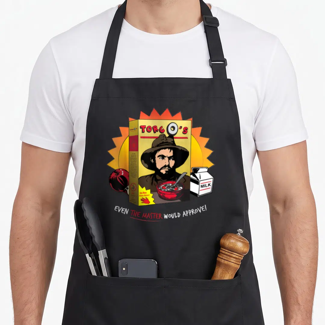 Torgo cereal apron - Cartoon cereal box with stern man, apple, milk carton, and text even the master would approve — shown on a black cotton canvas apron against a white background