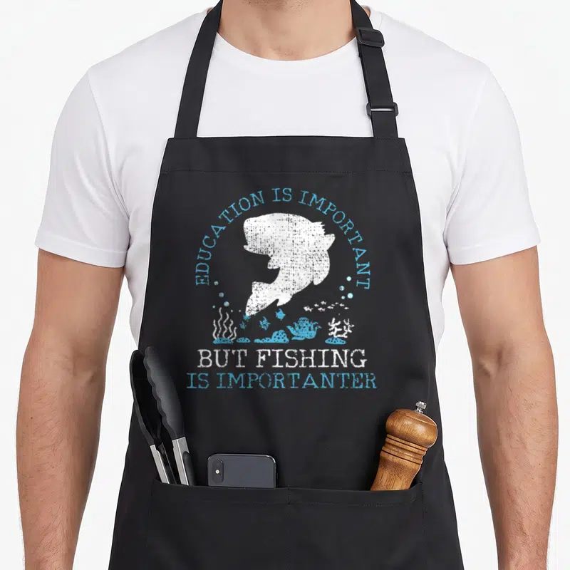 Fishing education apron - White fish silhouette under arched blue text with underwater plants and bubbles in distressed — shown on a black cotton canvas apron against a white background