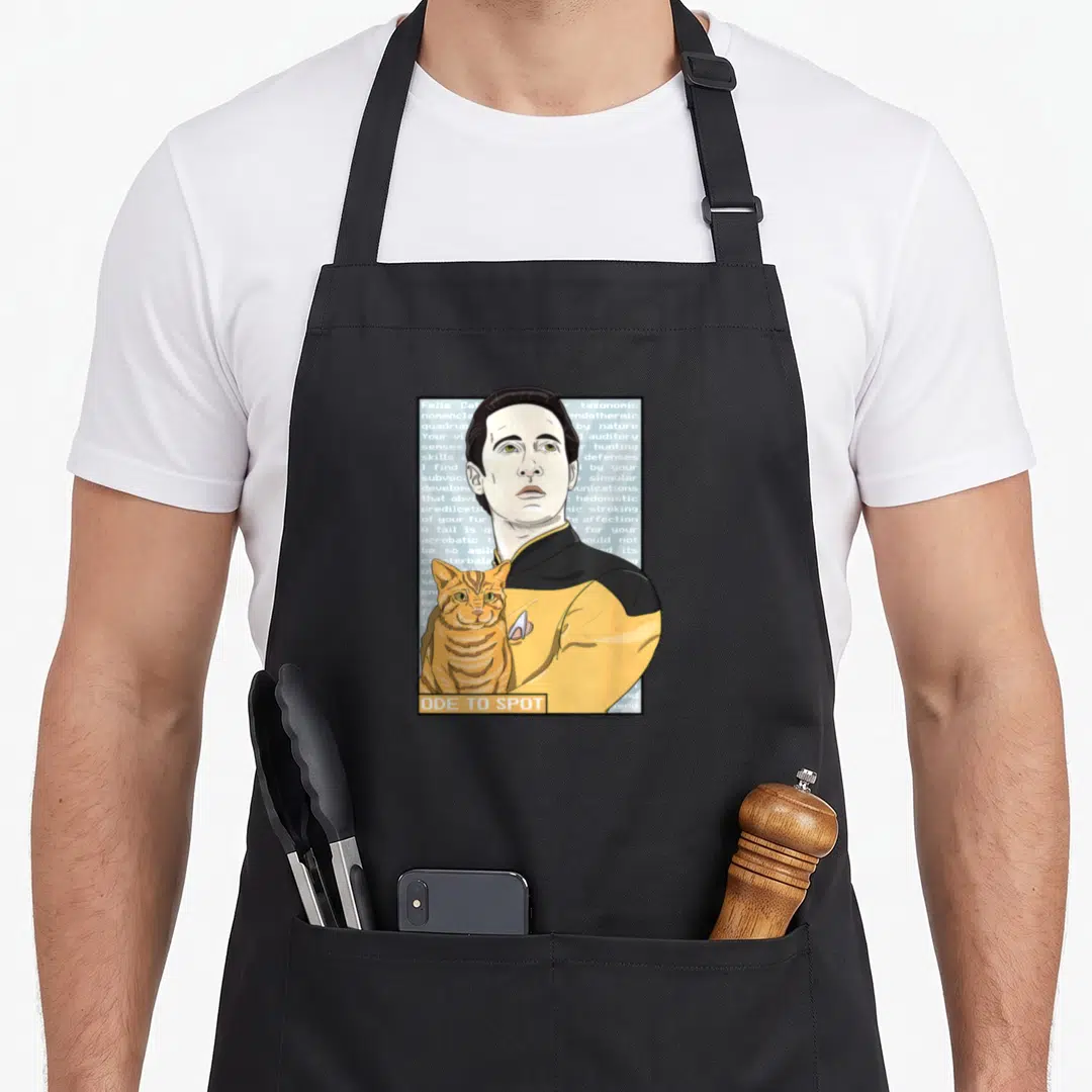 Generation data apron - Man in yellow uniform holding orange cat with Ode to Spot text banner — shown on a black cotton canvas apron against a white background