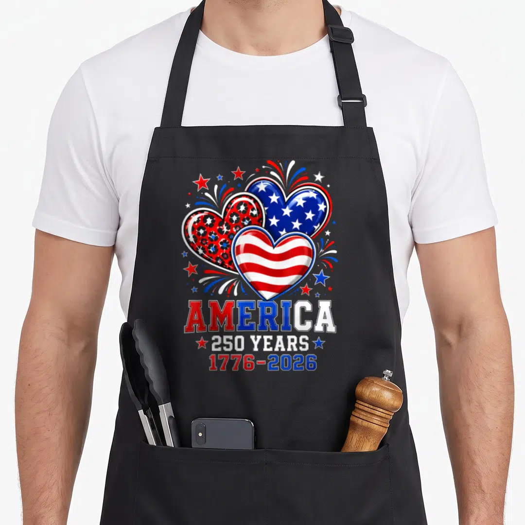 250th anniversary apron - Three hearts in red white and blue with fireworks and stacked text reading America 250 Years — shown on a black cotton canvas apron against a white background