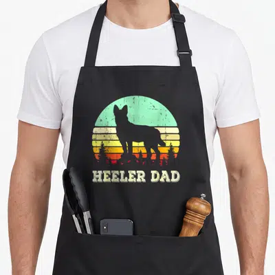 Blue father day apron - Grey dog silhouette against teal and yellow striped sun with HEELER DAD text below — shown on a black cotton canvas apron against a white background