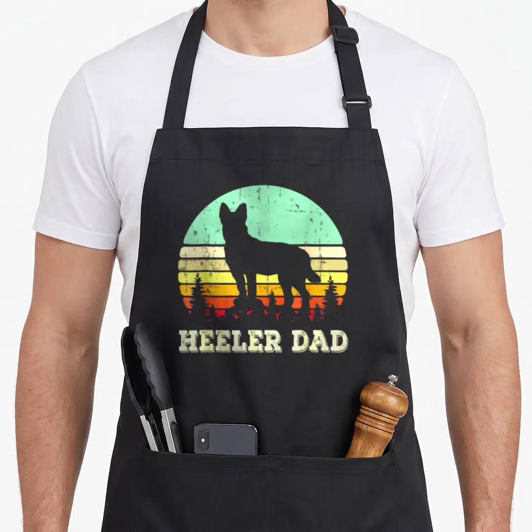 Blue father day apron - Grey dog silhouette against teal and yellow striped sun with HEELER DAD text below — shown on a black cotton canvas apron against a white background