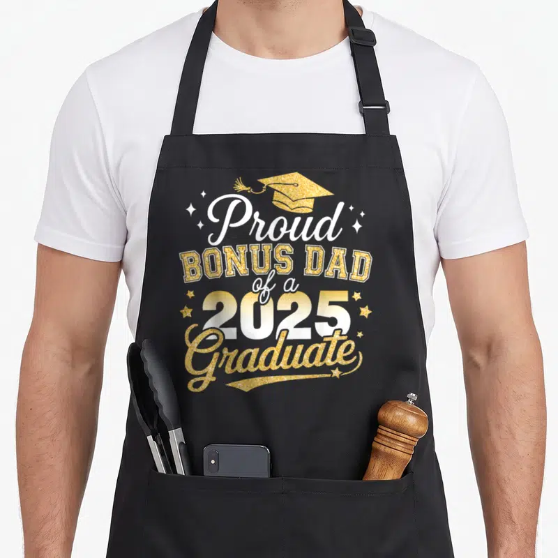 Bonus diploma apron - Gold graduation cap and white text Proud Bonus Dad 2025 Graduate with stars — shown on a black cotton canvas apron against a white background