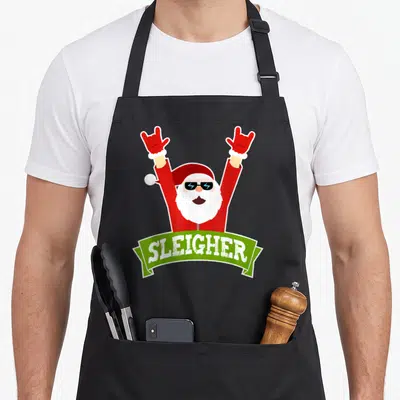 Sleigher heavy apron - Santa in red suit with sunglasses holding rock signs above green SLEIGHER banner — shown on a black cotton canvas apron against a white background
