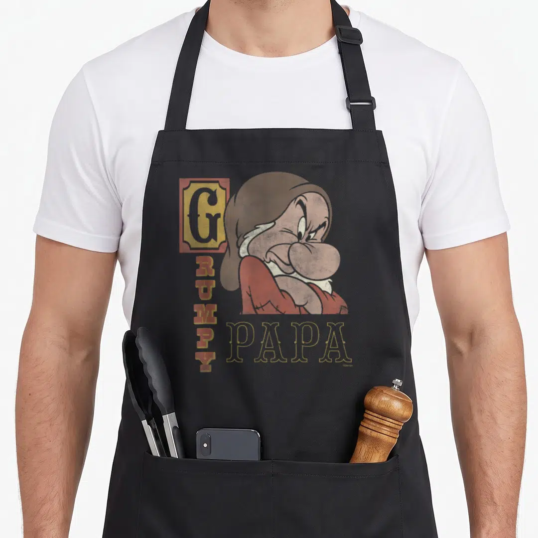 Snow papa apron - Grumpy dwarf illustration with vertical GRUMPY text and horizontal PAPA label in distressed style — shown on a black cotton canvas apron against a white background