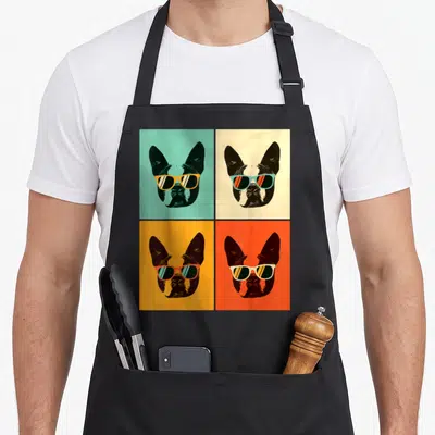 Bostie boston dog apron - Four dog heads in a grid on teal, beige, yellow, and orange backgrounds wearing sunglasses — shown on a black cotton canvas apron against a white background