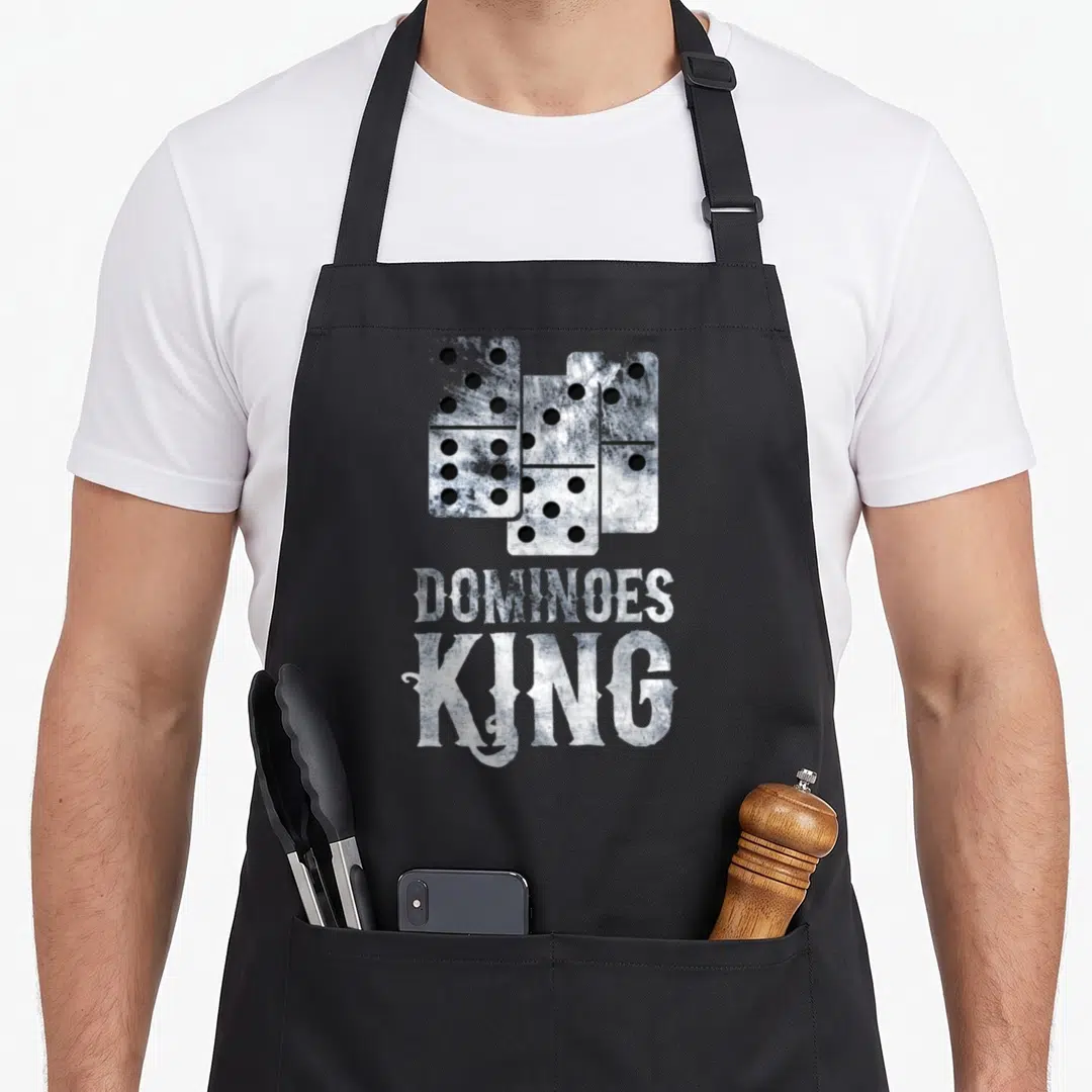 Tile king apron - Three distressed domino tiles above stacked DOMWOES KING text in white and grey — shown on a black cotton canvas apron against a white background