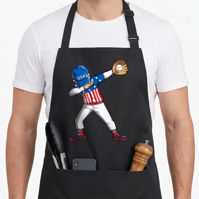 Player 4th of july apron - Cartoon baseball player dabbing in USA uniform holding glove with ball — shown on a black cotton canvas apron against a white background