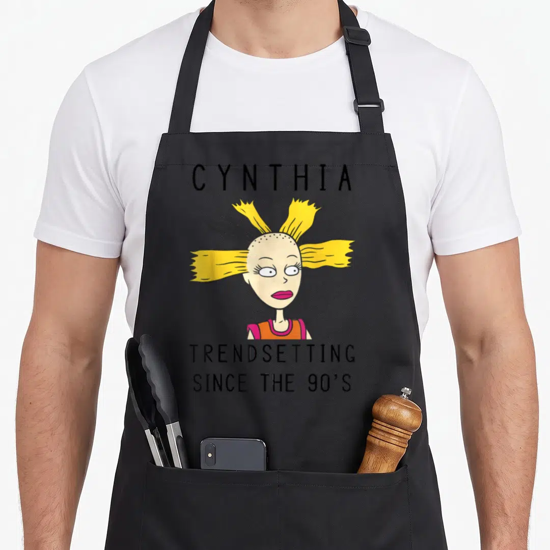 Cynthia 90s apron - Cartoon girl with spiky yellow hair and text CYNTHIA TRENDSETTING SINCE THE 90'S — shown on a black cotton canvas apron against a white background