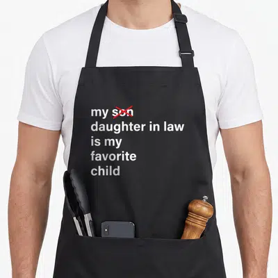 Funny law father day apron - White text reading my daughter in law is my favorite child with red cross over son — shown on a black cotton canvas apron against a white background