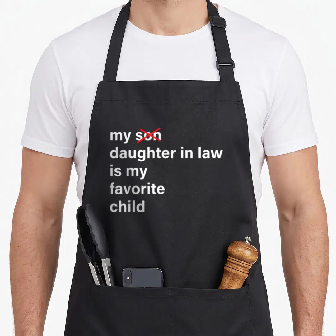 Funny law father day apron - White text reading my daughter in law is my favorite child with red cross over son — shown on a black cotton canvas apron against a white background