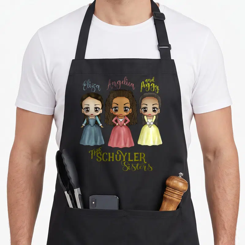 Sister kawaii apron - Three cartoon women in blue pink yellow dresses with names Eliza Angelica Peggy and THE SCHUYLER — shown on a black cotton canvas apron against a white background