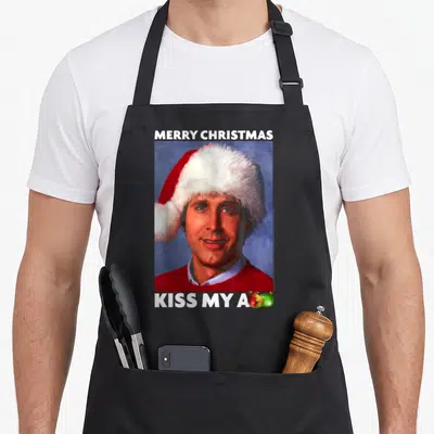 Vacation merry christmas apron - Man in Santa hat with Merry Christmas text and ornaments replacing final letter — shown on a black cotton canvas apron against a white background