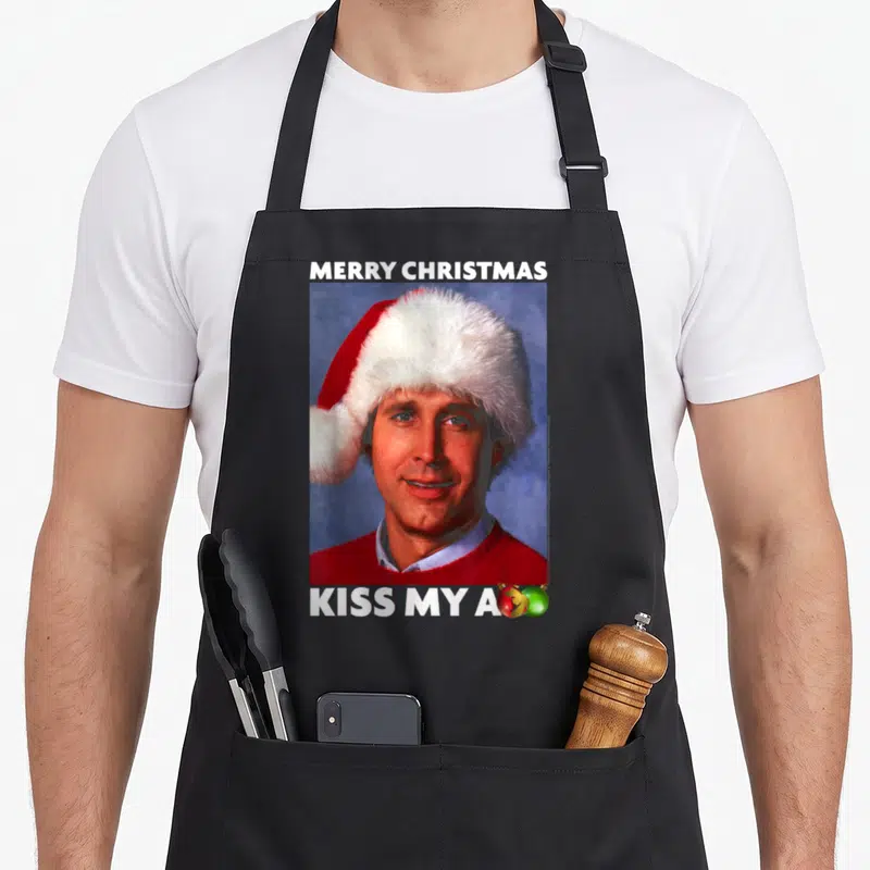 Vacation merry christmas apron - Man in Santa hat with Merry Christmas text and ornaments replacing final letter — shown on a black cotton canvas apron against a white background