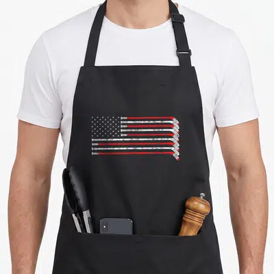 Stick hockey apron - USA flag formed by 13 red and white hockey sticks with blue star field and distressed texture — shown on a black cotton canvas apron against a white background