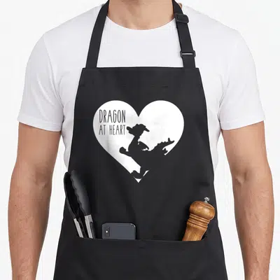 Retro dragon apron - Grey dragon silhouette inside white heart with text DRAGON AT HEART — shown on a black cotton canvas apron against a white background
