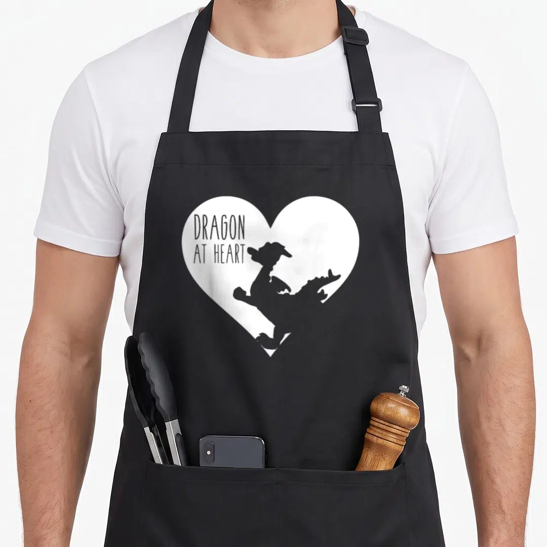 Retro dragon apron - Grey dragon silhouette inside white heart with text DRAGON AT HEART — shown on a black cotton canvas apron against a white background