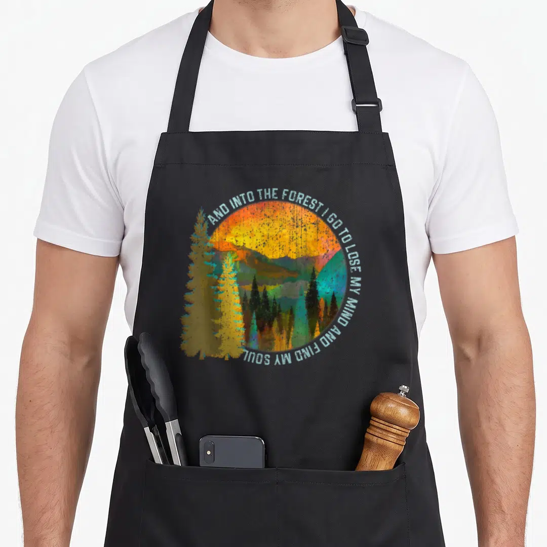 Nature camping apron - Retro forest landscape with circular text arch AND INTO THE FOREST I GO TO LOSE MY MIND AND FIND — shown on a black cotton canvas apron against a white background