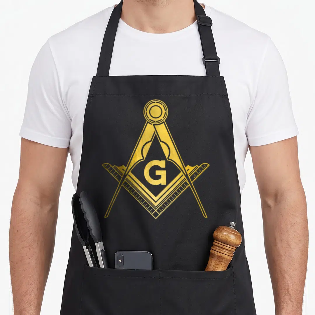 Compass masonic mason apron - Gold square and compass symbol with a centered G letter on black fabric — shown on a black cotton canvas apron against a white background