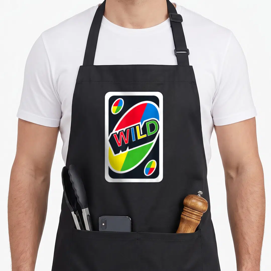 Uno wars new apron - Black card with white border, multi-colored WILD text, and four-color ovals — shown on a black cotton canvas apron against a white background