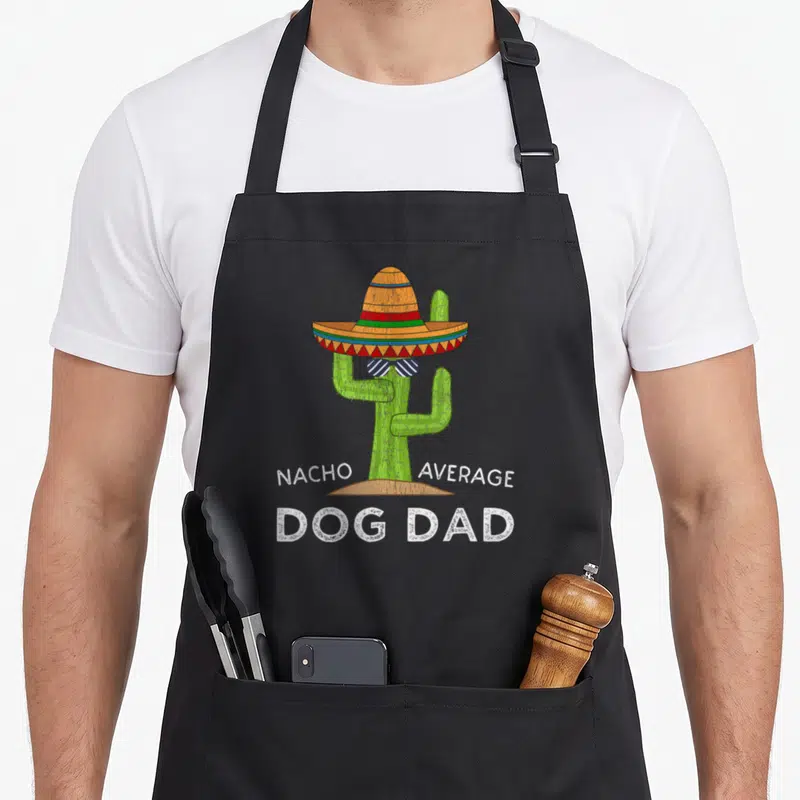 Dog custom pet apron - Cartoon cactus in sombrero and sunglasses with Nacho Average Dog Dad text — shown on a black cotton canvas apron against a white background