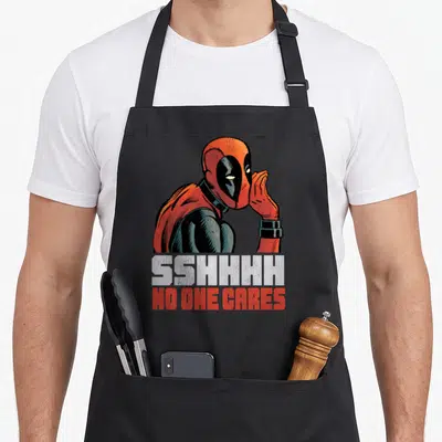 Shhh care apron - Deadpool whispering above text SSHHHH NO ONE CARES in red and grey — shown on a black cotton canvas apron against a white background