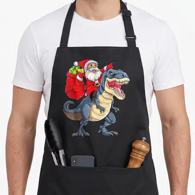 Dinosaur christmas santa apron - Santa Claus riding a blue T-Rex holding a red sack of gifts in a cartoon style — shown on a black cotton canvas apron against a white background