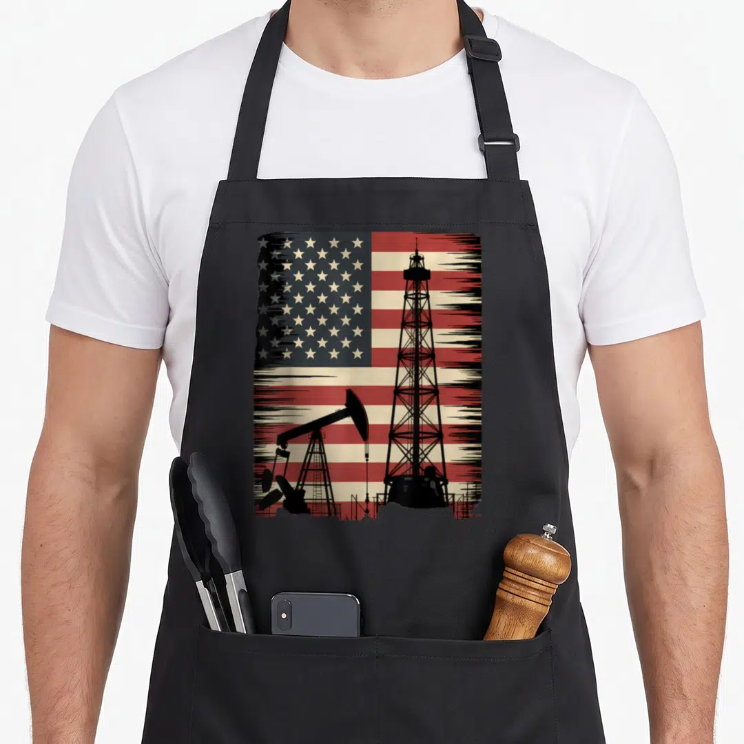 Oilman big rig apron - Black oil rig and pumpjack silhouettes over a distressed red white and blue USA flag — shown on a black cotton canvas apron against a white background