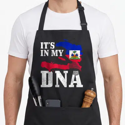 Haiti dna pride apron - Distressed Haiti map in blue and red with IT'S IN MY DNA text and fingerprint graphic — shown on a black cotton canvas apron against a white background