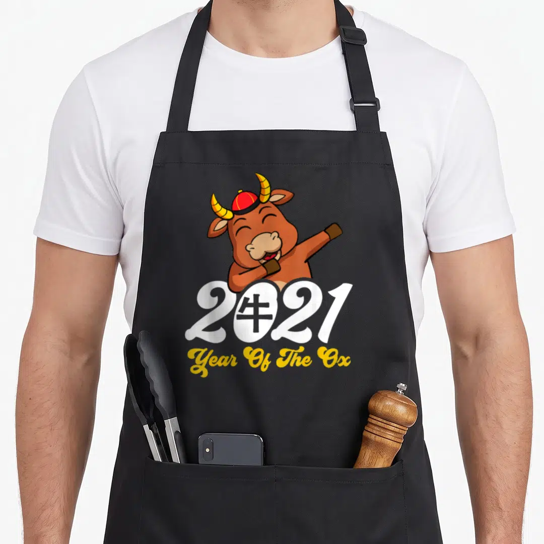 Chinese horoscope zodiac aprons - Cartoon ox in red hat behind white 2021 text and yellow script — shown on a black cotton canvas apron against a white background