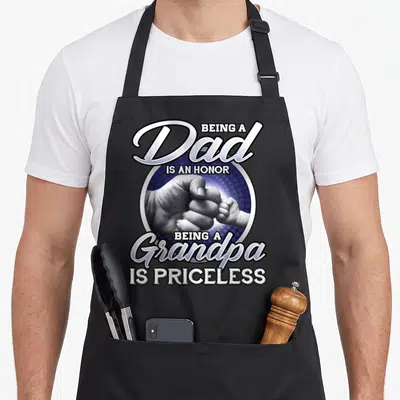 Funny honor grandpa apron - Dad Grandpa text above and below a fist bump photo of an adult hand and baby hand on a blue — shown on a black cotton canvas apron against a white background