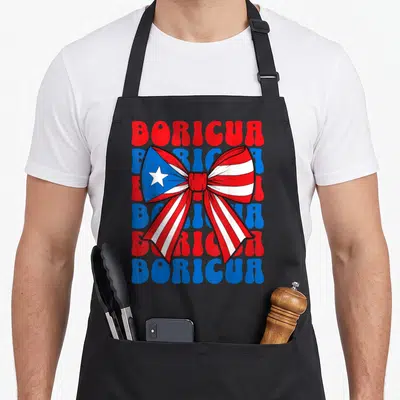 Boricua bow apron - Large bow with Puerto Rican flag pattern over six alternating red and blue BORICUA text lines — shown on a black cotton canvas apron against a white background