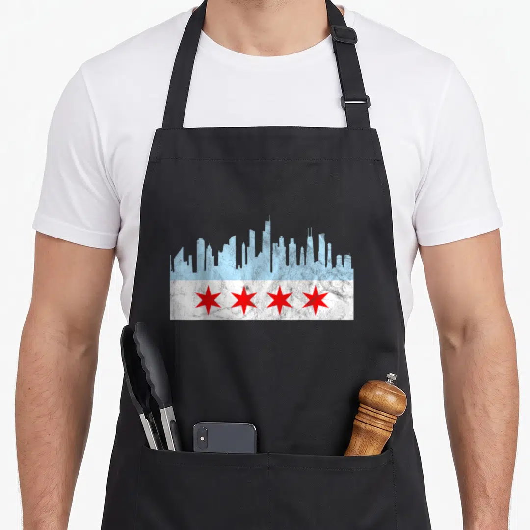 Flag distressed chicago apron - Light blue skyline silhouette above four red stars on a white distressed band — shown on a black cotton canvas apron against a white background