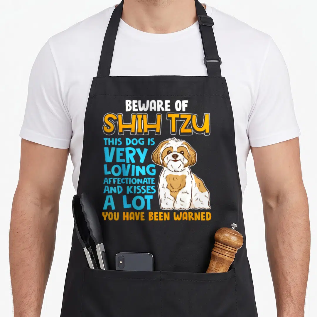 Shih lion apron - Cartoon Shih Tzu with Beware of Shih Tzu text in orange blue and white — shown on a black cotton canvas apron against a white background
