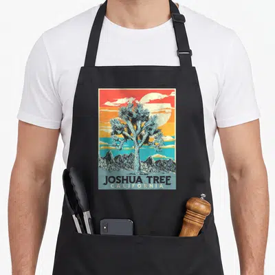 Joshua artistic apron - Retro blue Joshua tree against red orange yellow and blue sunset bands with California text — shown on a black cotton canvas apron against a white background