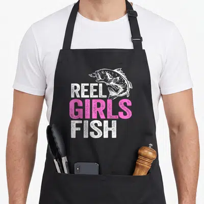 Fisherwoman fish apron - Distressed white and pink Reel Girls Fish text with bass fish graphic — shown on a black cotton canvas apron against a white background