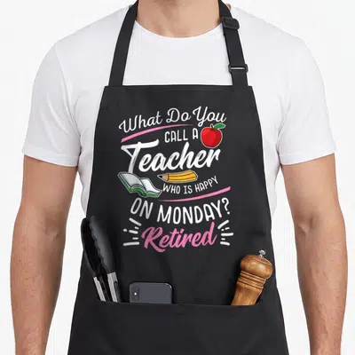 Monday teachers apron - Text reading What Do You Call A Teacher Who Is Happy On Monday Retired with apple and book — shown on a black cotton canvas apron against a white background