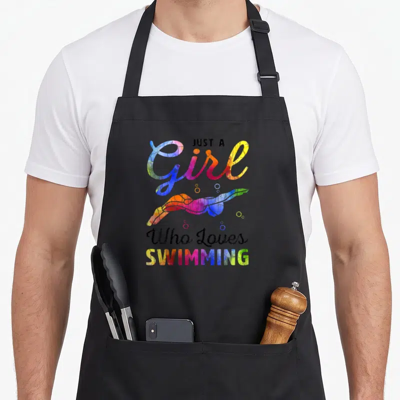 Swimming swimmer apron - Just A Girl Who Loves Swimming text with watercolor swimmer and bubbles in blue pink yellow — shown on a black cotton canvas apron against a white background
