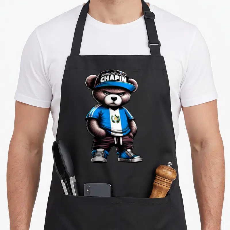 Unapologetically guatemalan apron - Cartoon bear in blue white flag shirt and cap reading Unapologetically Chapin — shown on a black cotton canvas apron against a white background